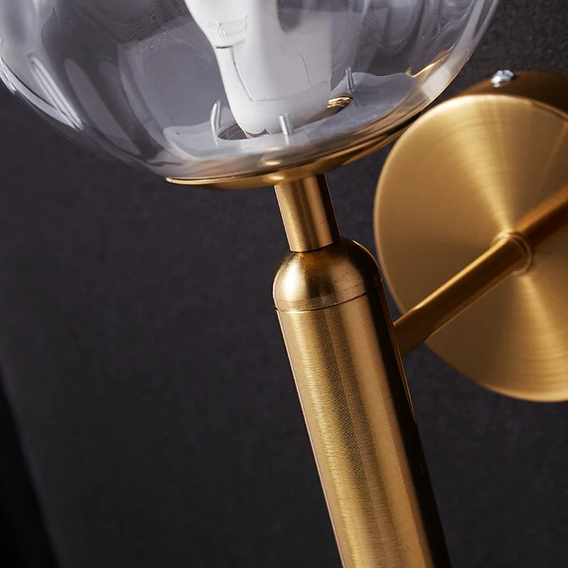 Luminaire moderne industriel doré en verre clair, globe élégant fixé sur un mur sombre.