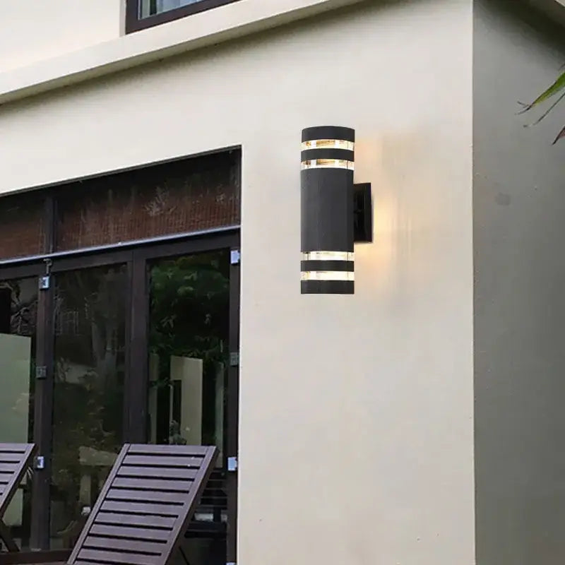 Luminaire LED cylindrique en acier brossé fixé sur un mur crème.