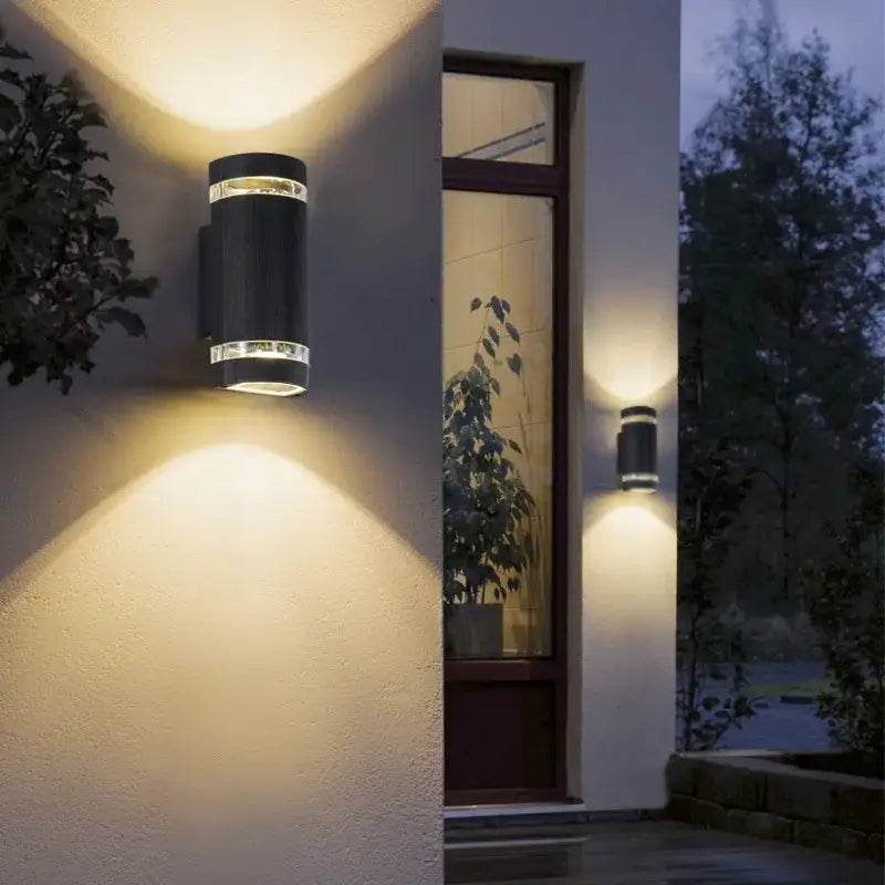 Applique murale extérieure LED cylindrique en acier brossé, émet une lumière douce au crépuscule.