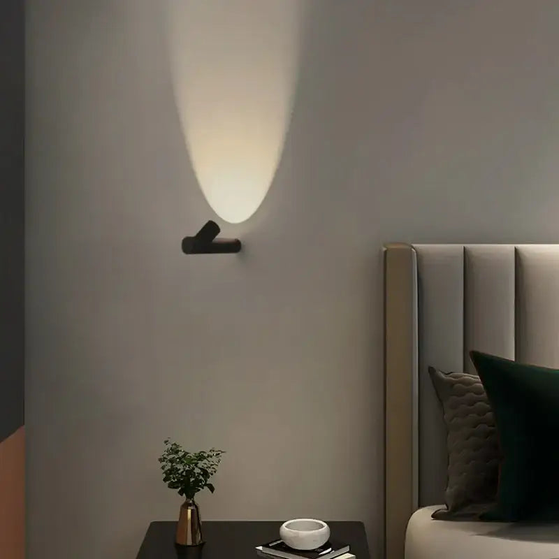Applique murale LED noire design contemporain diffusant une lumière chaude vers le haut sur un mur gris.