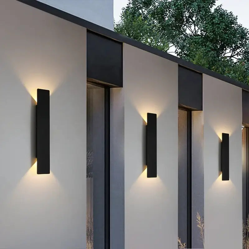Applique murale extérieur noire projette une lumière douce et symétrique sur un mur moderne.