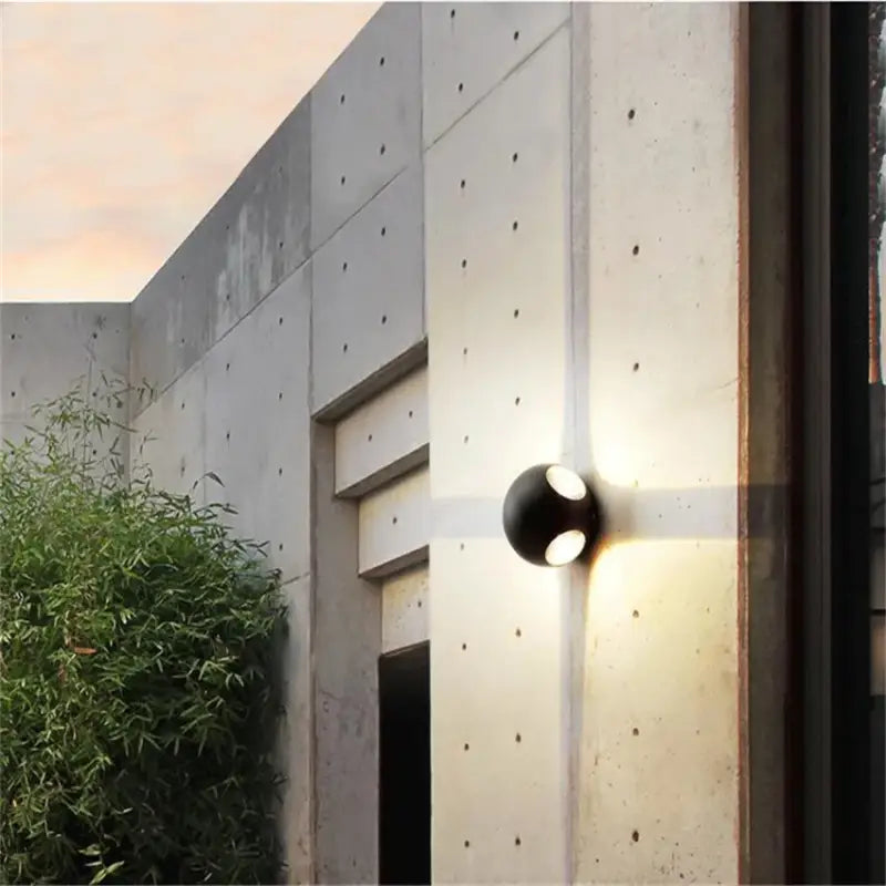 Applique murale aluminium LED boule moderne, éclairage multidirectionnel, installée sur mur béton.
