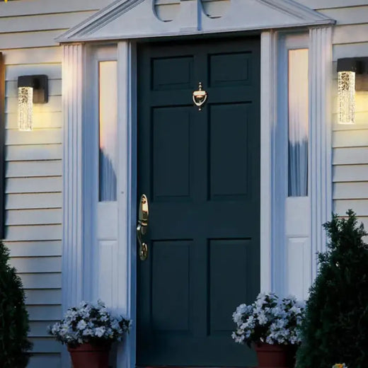 Luminaires muraux extérieurs Cristal Aluminium diffusant une lumière douce de chaque côté de la porte.