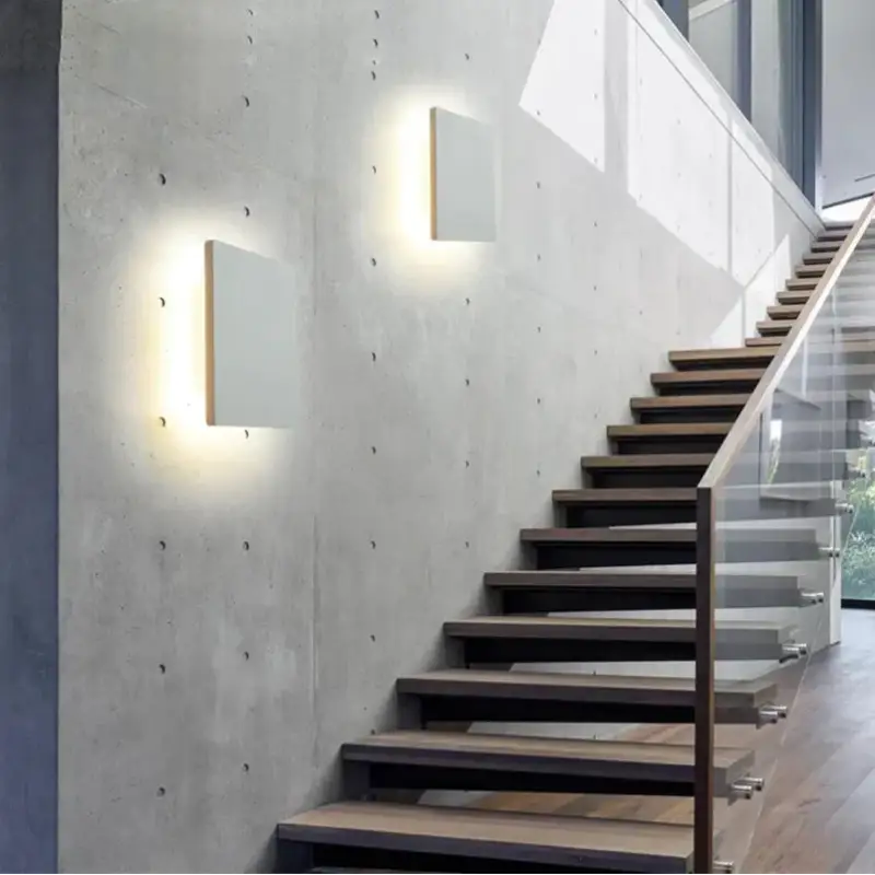 Deux luminaires muraux carrés en aluminium, éclairage doux sur mur en béton, style moderne.