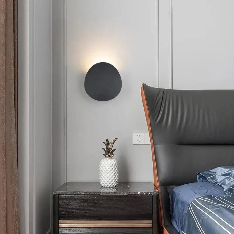 Luminaire mural rond en aluminium LED éclaire élégamment une tête de lit grise.
