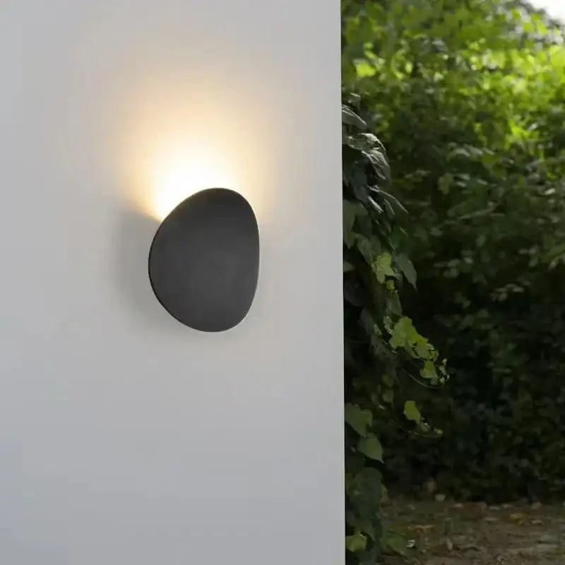 Luminaire mural LED rond en aluminium diffusant une lumière chaude sur un mur blanc.