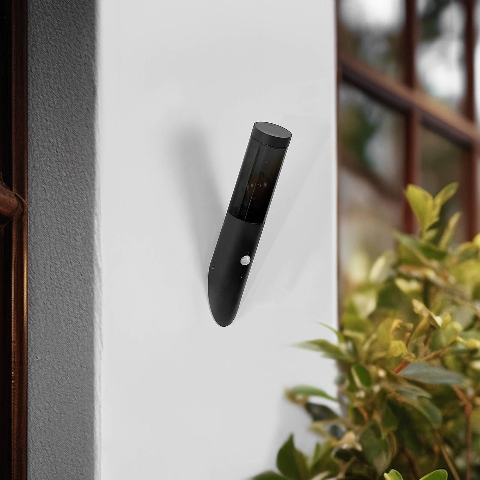 Applique murale extérieure noire avec détecteur de mouvement, fixée sur un mur blanc.
