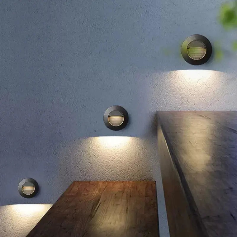Trois appliques murales rondes en aluminium diffusent une douce lumière LED sur un mur clair.